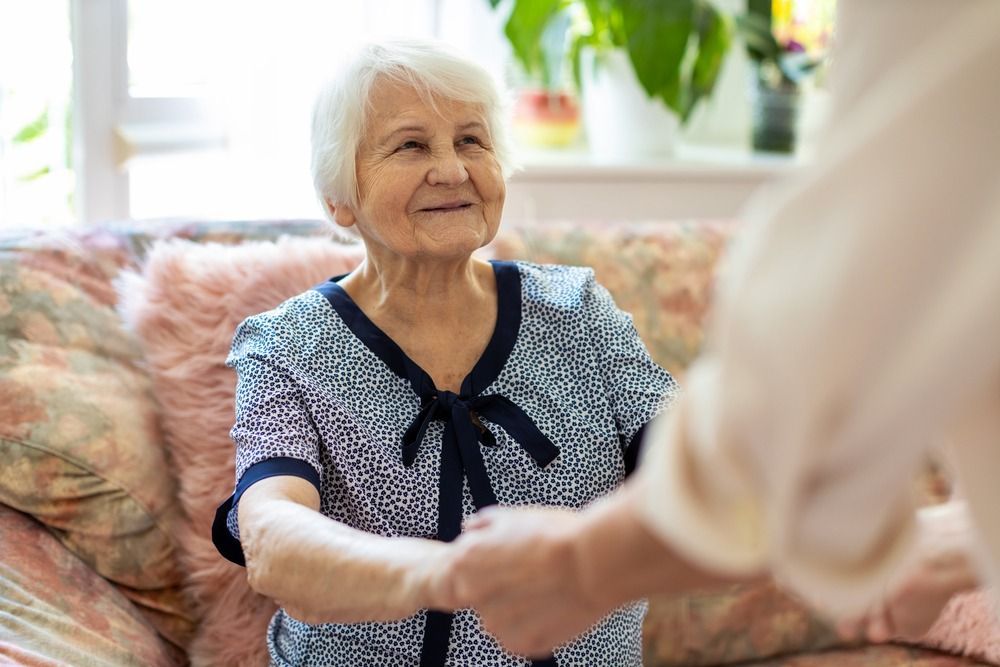 An elderly woman is sitting on a couch shaking hands with another woman.