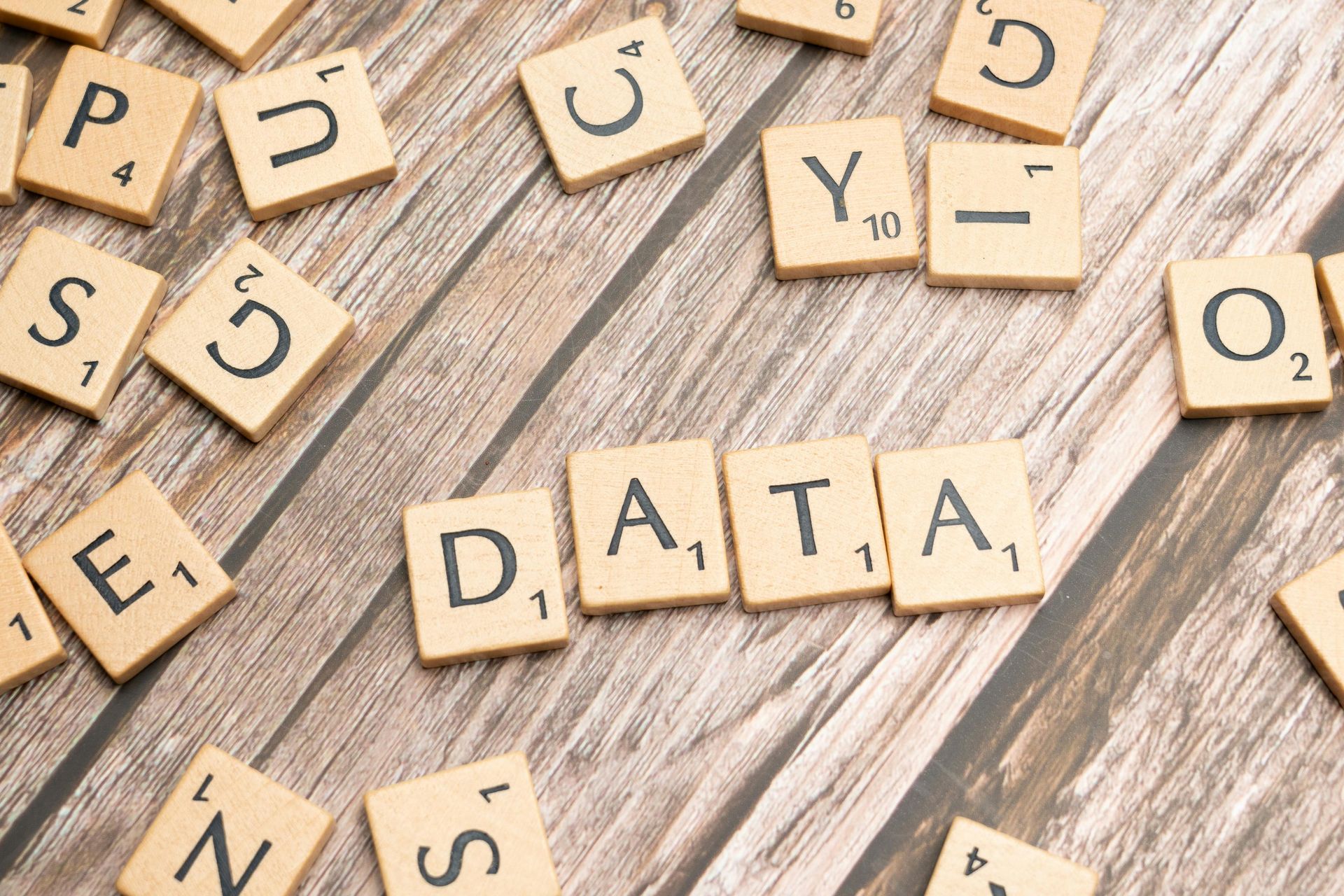 Wooden letter tiles spelling “DATA” on a light wood surface with scattered tiles around them