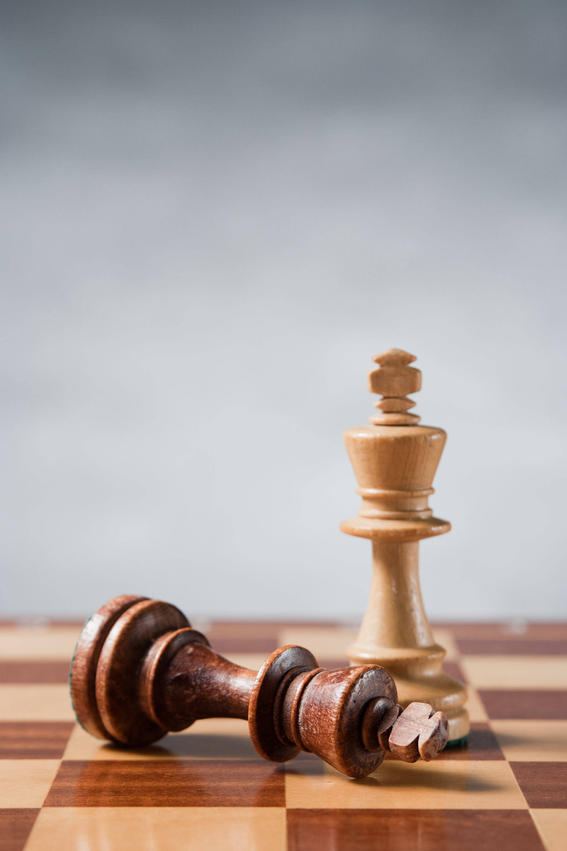 Two wooden chess pieces , a king and a queen , are on a chess board.