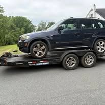 Blue car being towed on a trailer on a highway. The car is dark blue.