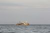 Fishing boat on calm water under a cloudy sky. The boat is light-colored and has various equipment visible.