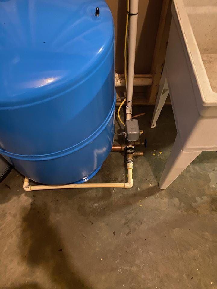 A blue water tank is sitting next to a white sink in a basement.