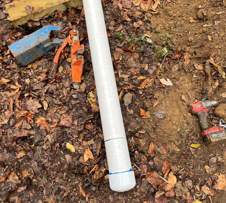 A white pipe is laying on the ground next to a drill.