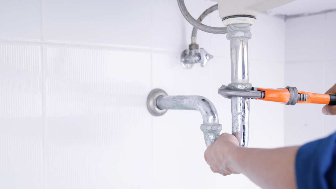 A plumber is fixing a sink pipe with a wrench.