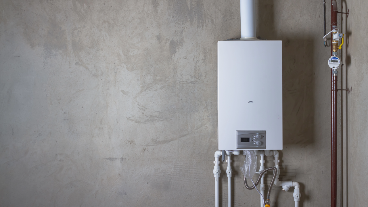 A white boiler is hanging on a wall next to pipes.