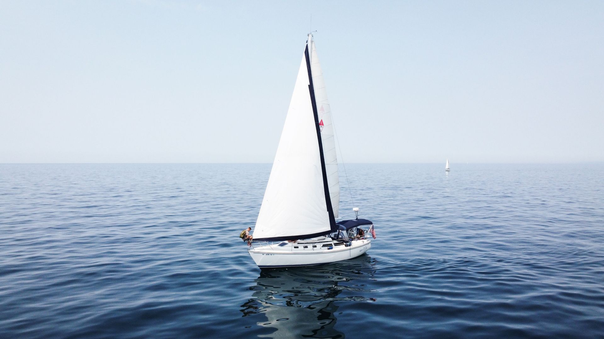 White sailboat gliding on calm blue sea under a clear sky