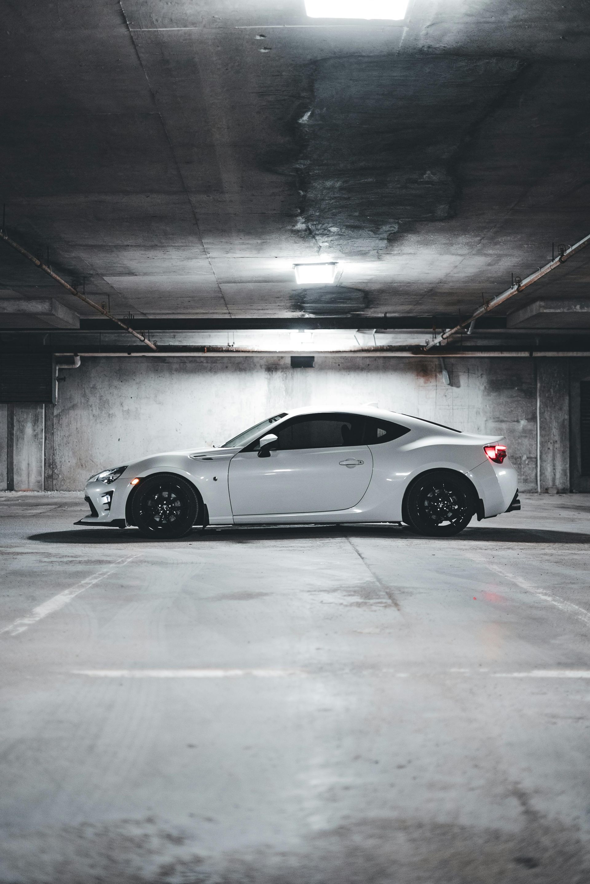 White sports car parked in a concrete parking garage, under bright ceiling lights.