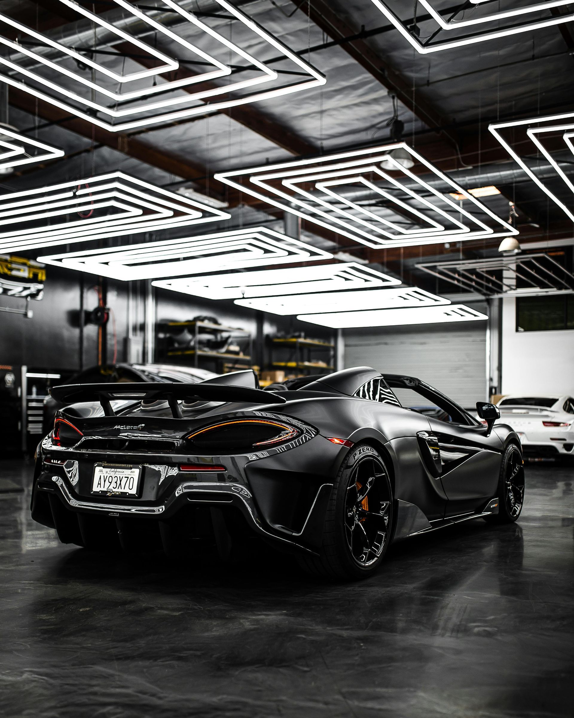Black McLaren sports car in a garage under geometric lights.