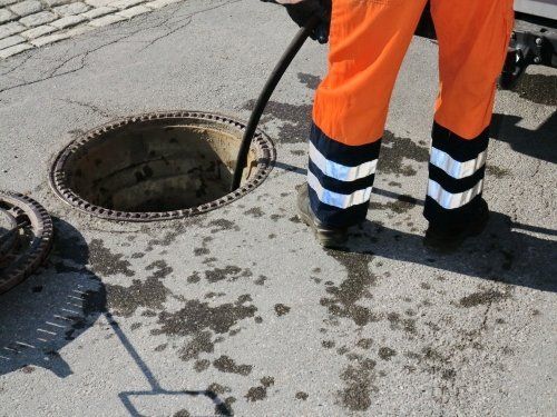 sewerage worker on street cleaning pipe