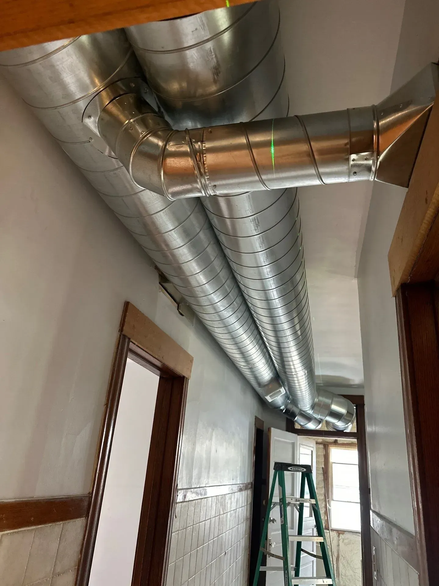 Galvanized metal HVAC ductwork runs across a hallway ceiling.