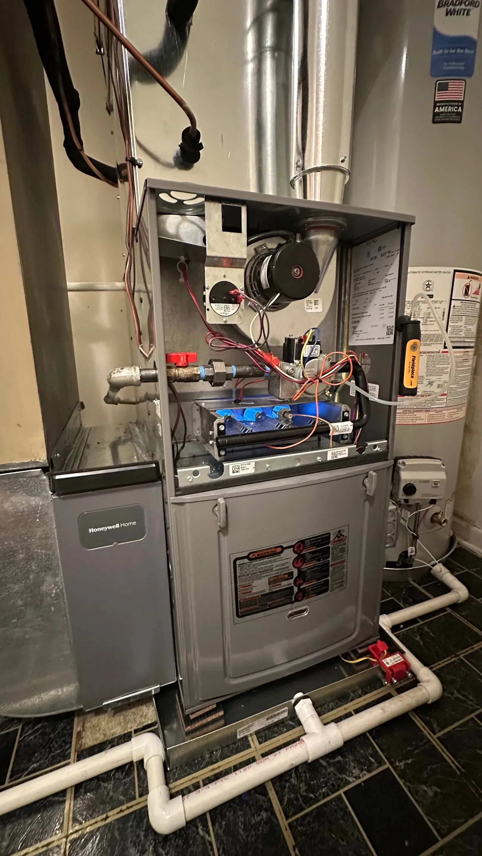 A furnace with blue flames burning, open for inspection.  Gas and ventilation pipes are visible.