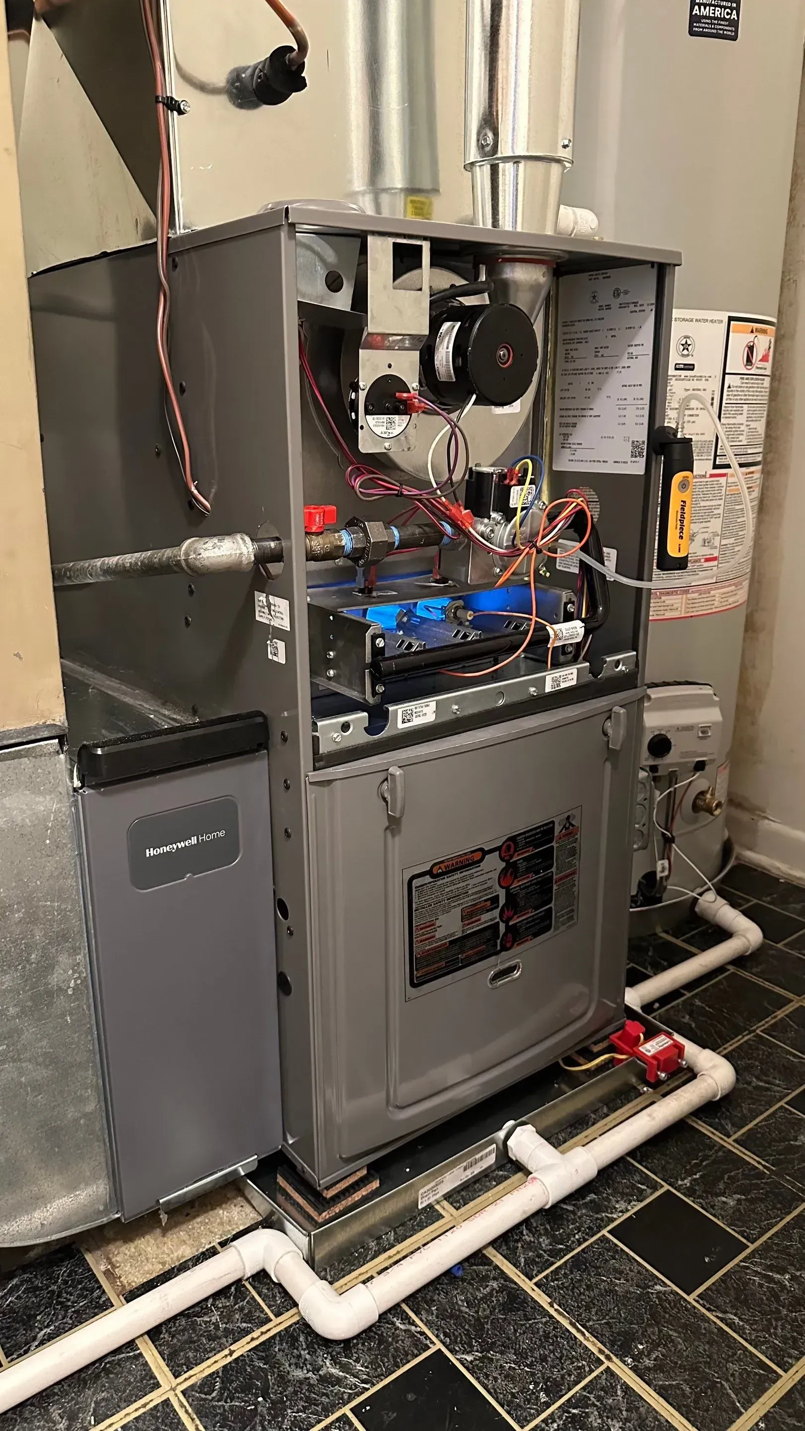 A furnace, grey metal cabinet, with open panels revealing components and wiring, in a basement.