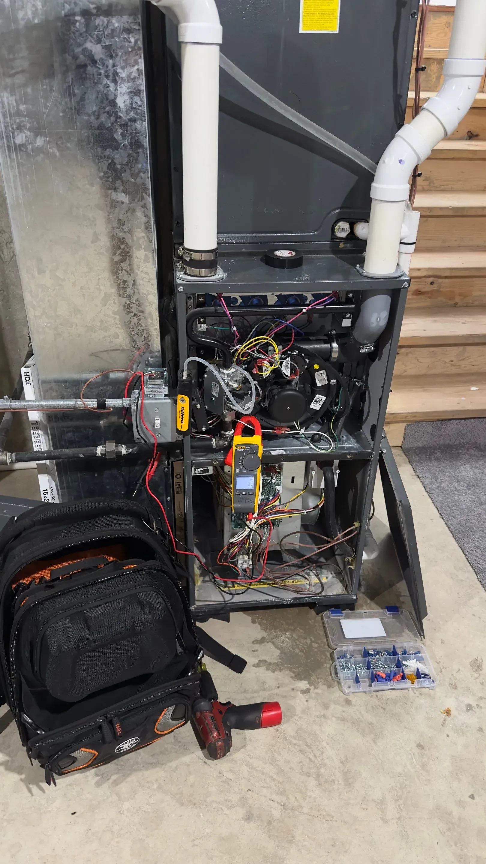 Furnace with open panels, wires, and a multimeter. A toolbox and tools are nearby.