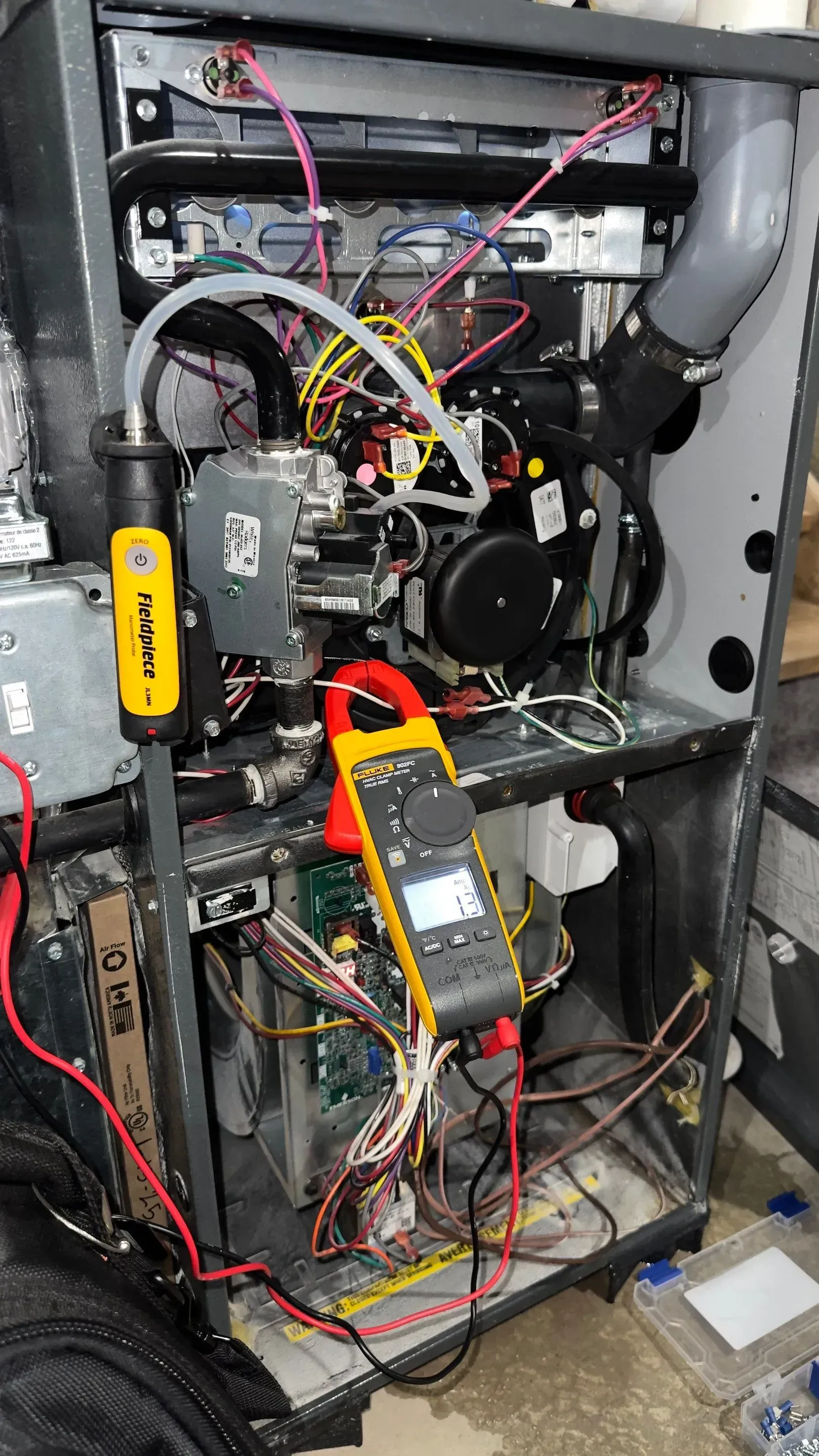 Furnace interior with digital multimeter attached to wiring, being serviced.
