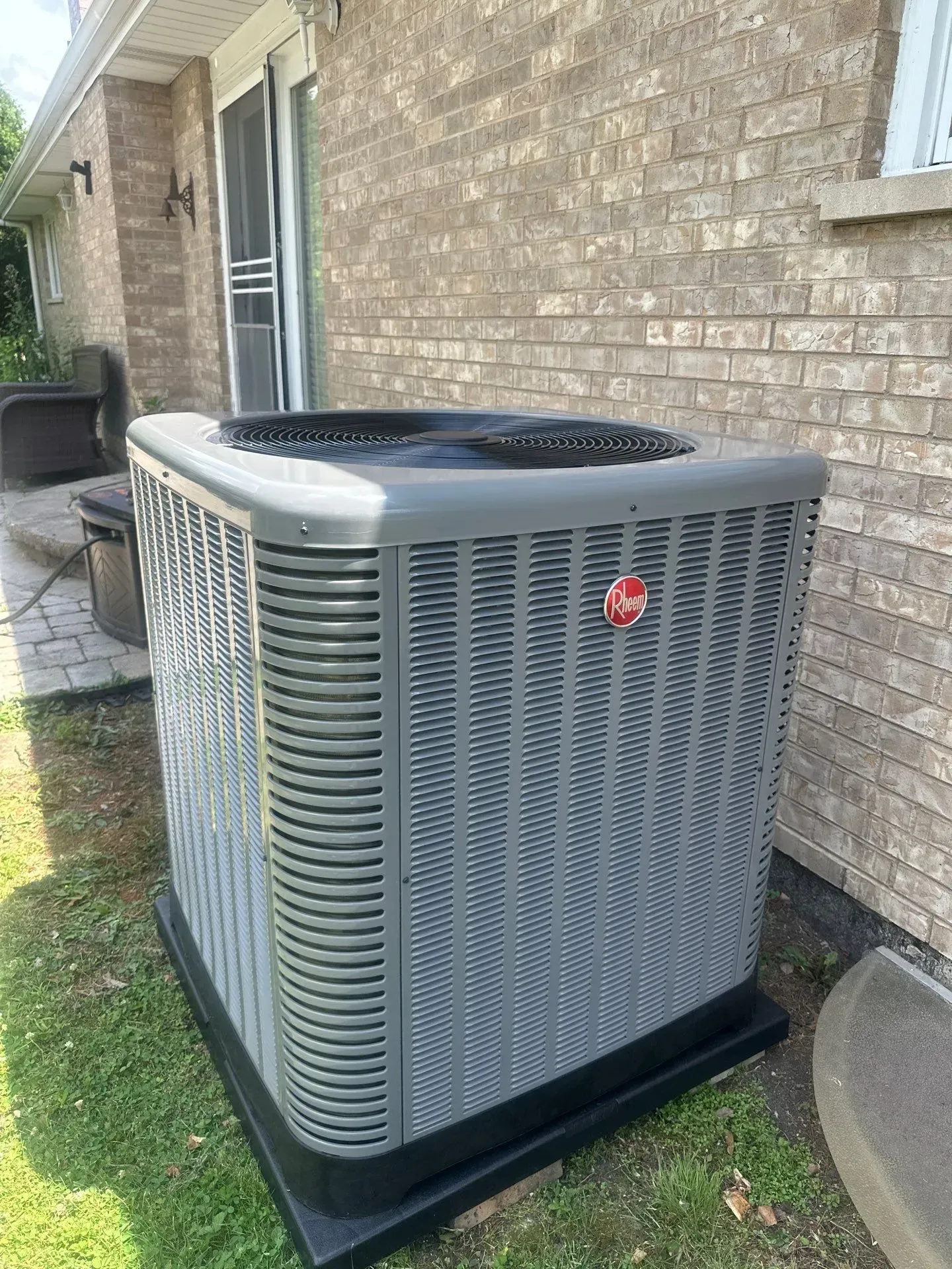 Air conditioning unit outside a brick building on green grass.