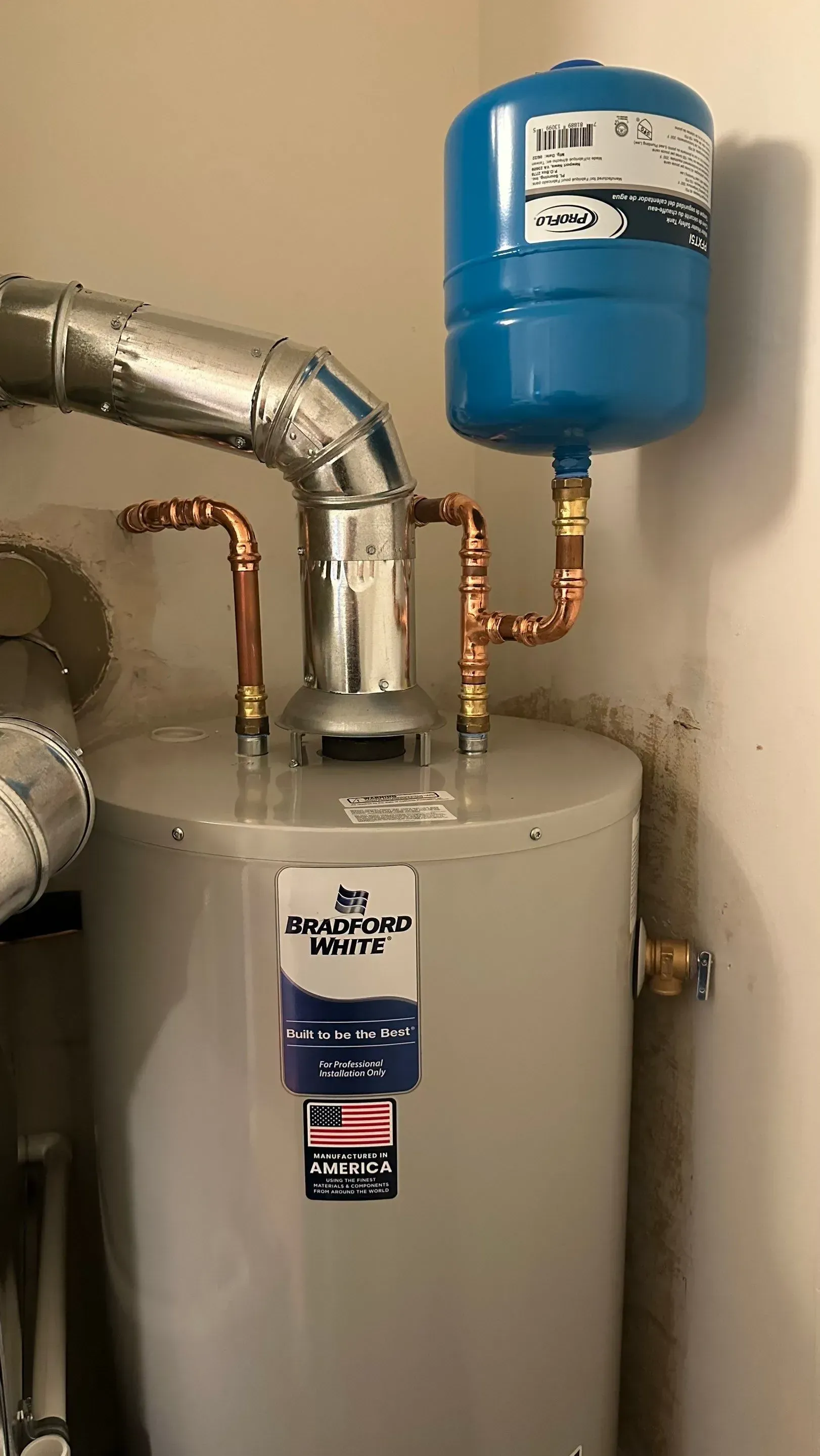 A water heater with a blue expansion tank, connected with copper pipes.  A silver vent pipe is also attached.