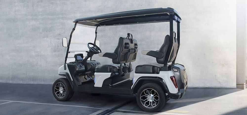 White golf cart with black roof and seats, parked against a concrete wall.