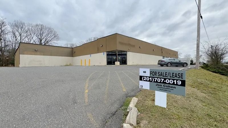 Empty warehouse building with a for-sale/lease sign in front on a gravel lot