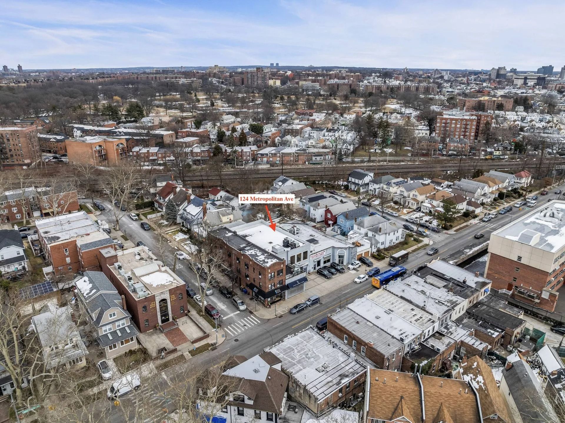 Aerial view of a snowy suburban neighborhood with houses, streets, and distant hills under a cloudy sky