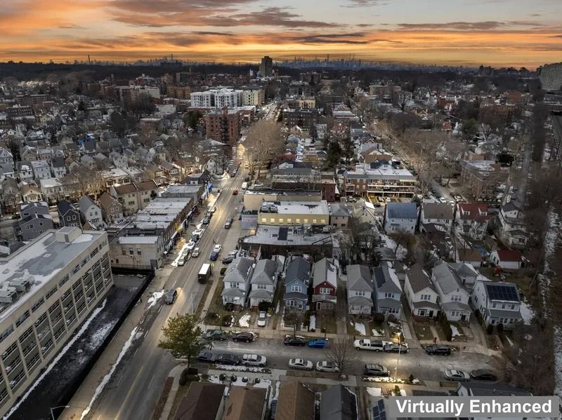 Aerial view of a snowy city at sunset, with traffic on a main road and orange sky on the horizon
