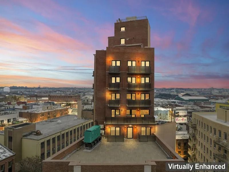 Tall brick building at sunset with lit windows above a city skyline and pink-blue sky