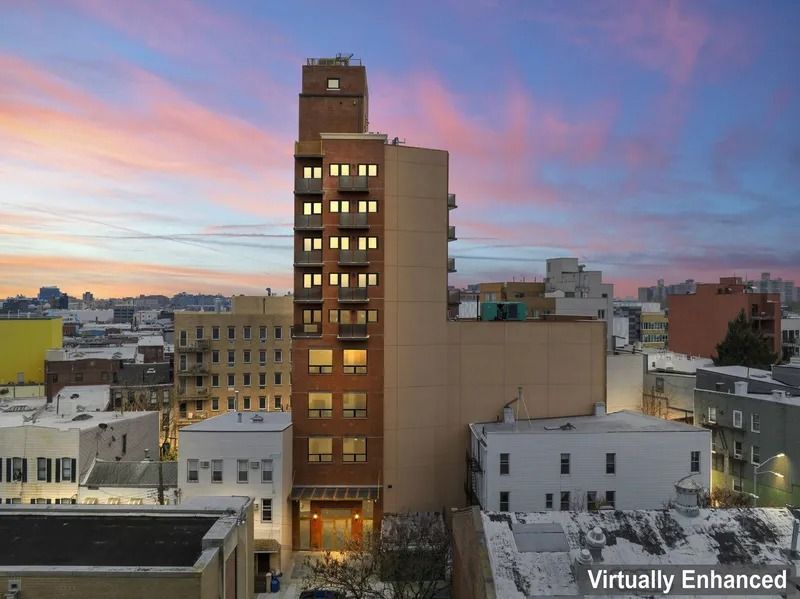 City skyline at sunset with a tall brick building lit by warm windows against a pink-blue sky