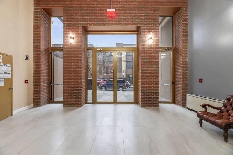 Brick building lobby with glass entrance doors, white floor, and a bench on the right.