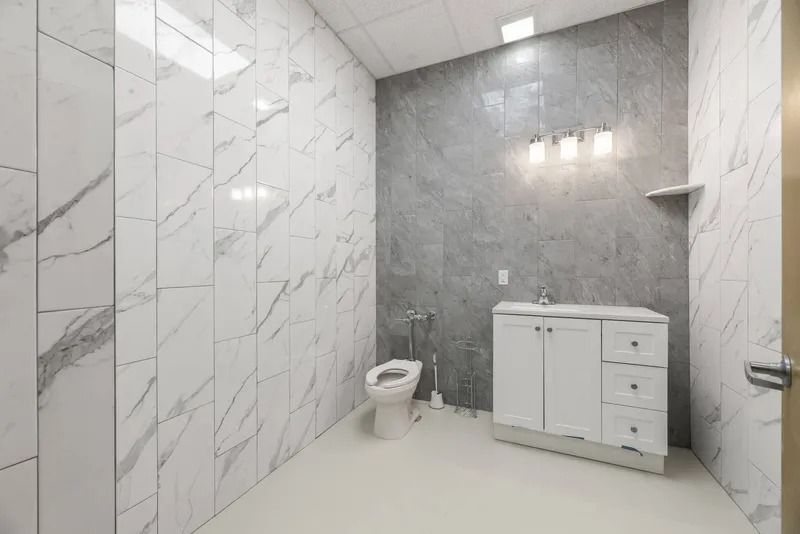 Modern bathroom with marble walls, gray accent wall, white vanity, toilet, and glass shower stall