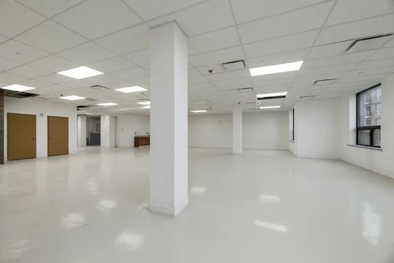 Empty white office room with columns, ceiling lights, doors, and windows