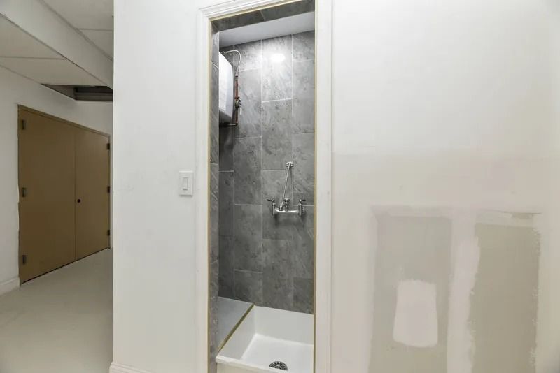 Bathroom alcove with tiled shower and white wall in a hallway on the left