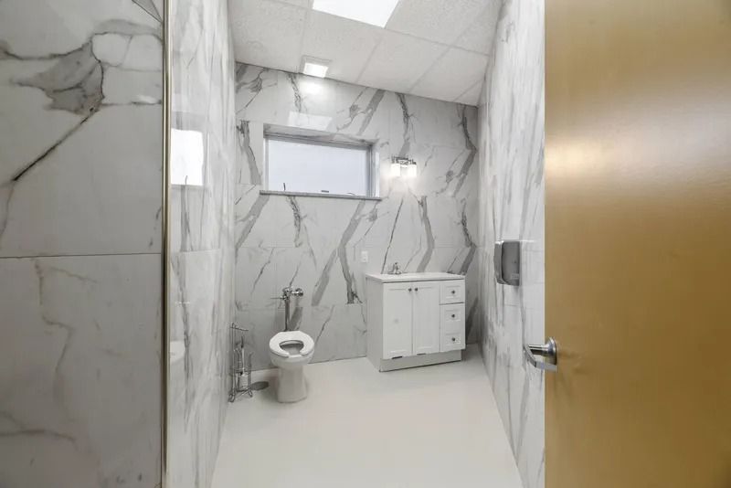 Modern bathroom with marble walls, white floor, toilet, vanity cabinet, and partially open wooden door