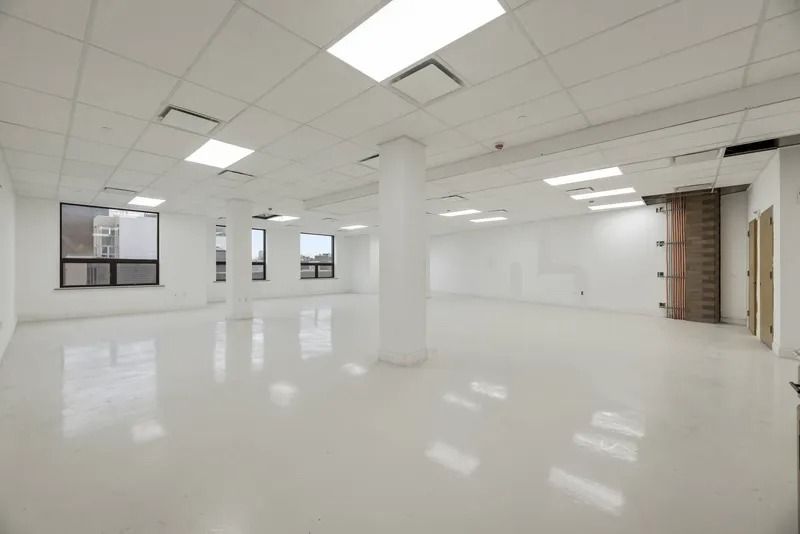 Empty white office space with tiled ceiling, columns, windows, and glossy floor