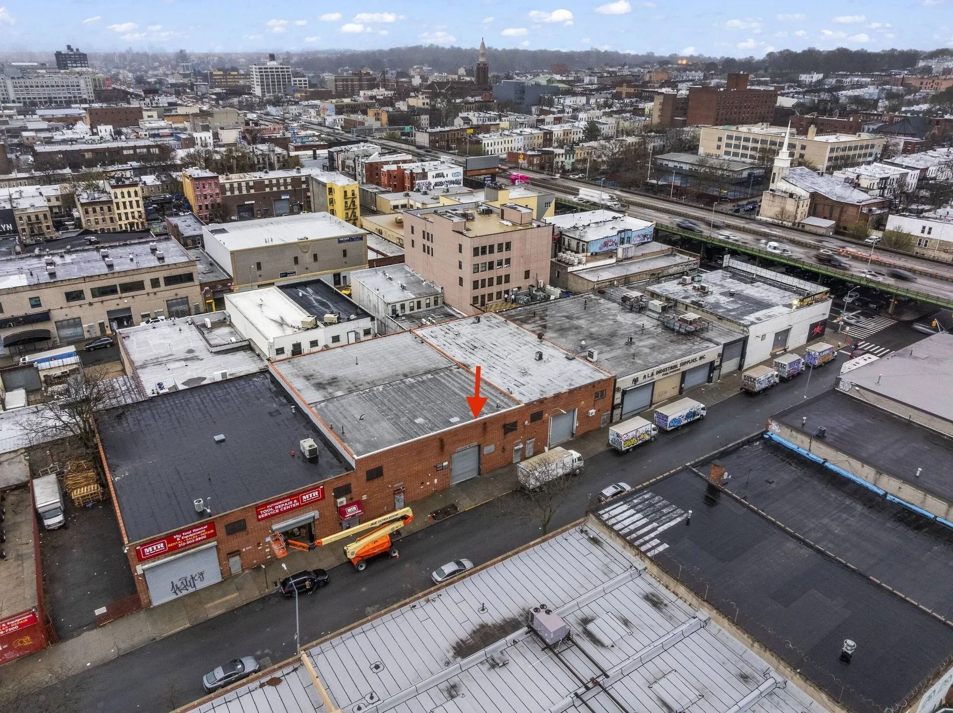 Aerial view of a snowy city block with low-rise buildings, streets, and rooftops under a cloudy sky
