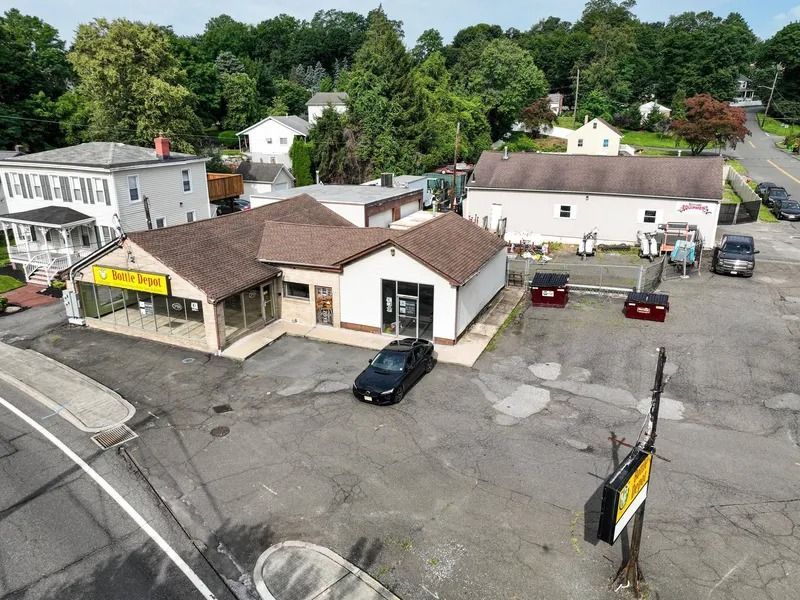 Aerial view of a small commercial building and parking lot with several cars, surrounded by trees.