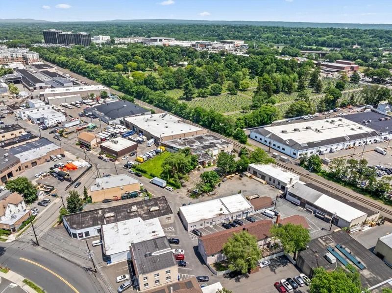 Aerial view of an industrial area with warehouses, parking lots, and green trees beyond.