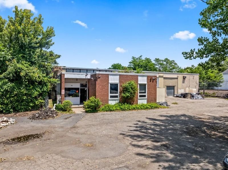 Abandoned brick building with boarded windows and overgrown trees under a blue sky