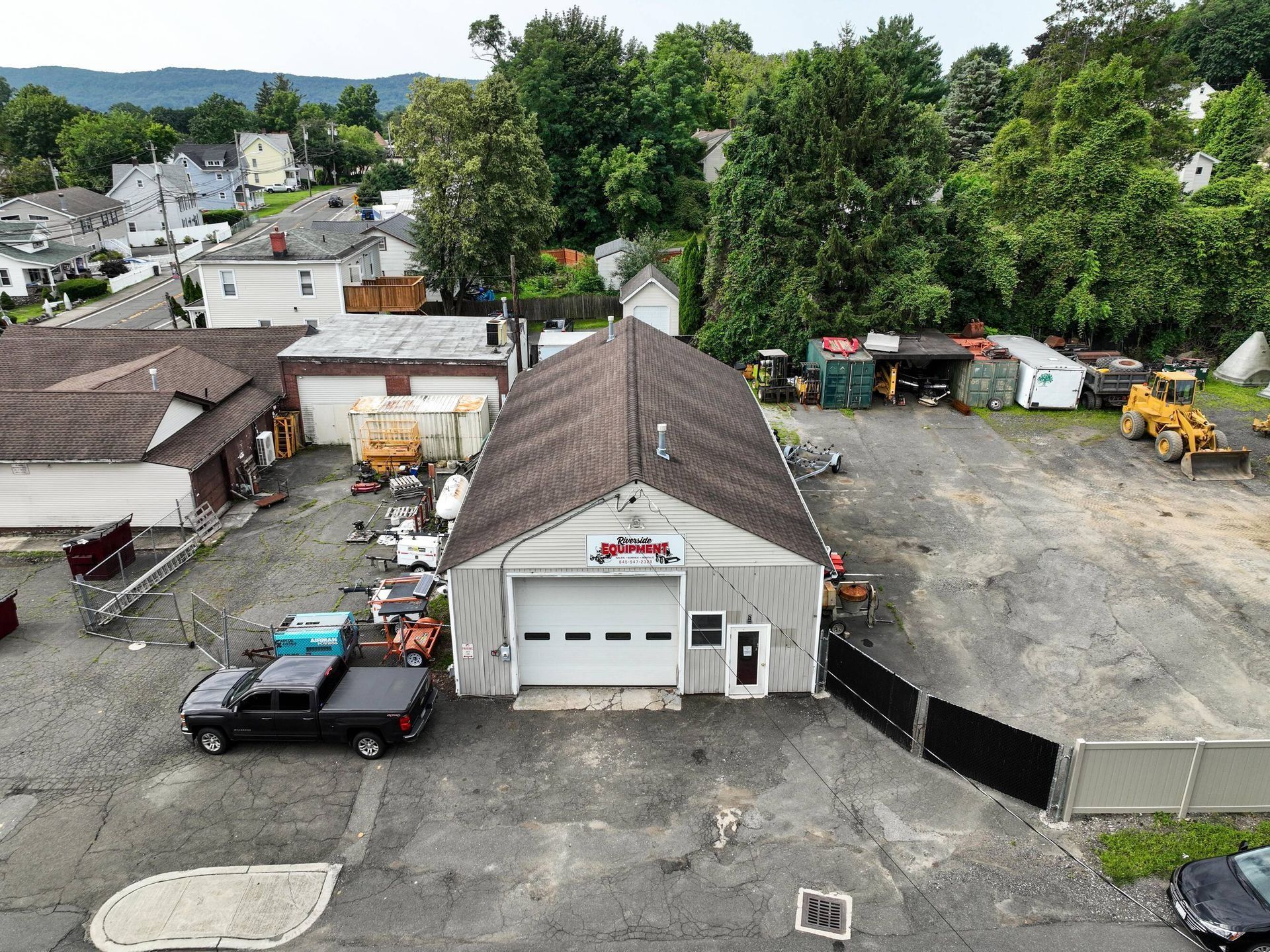 Small auto repair shop with parking lot, trucks, and equipment beside a tree-lined residential area