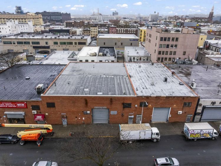 Aerial view of snowy city rooftops with brick warehouses and parked trucks on a street below