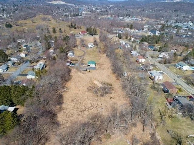 Aerial view of a grassy vacant lot bordered by houses and bare trees in a neighborhood.