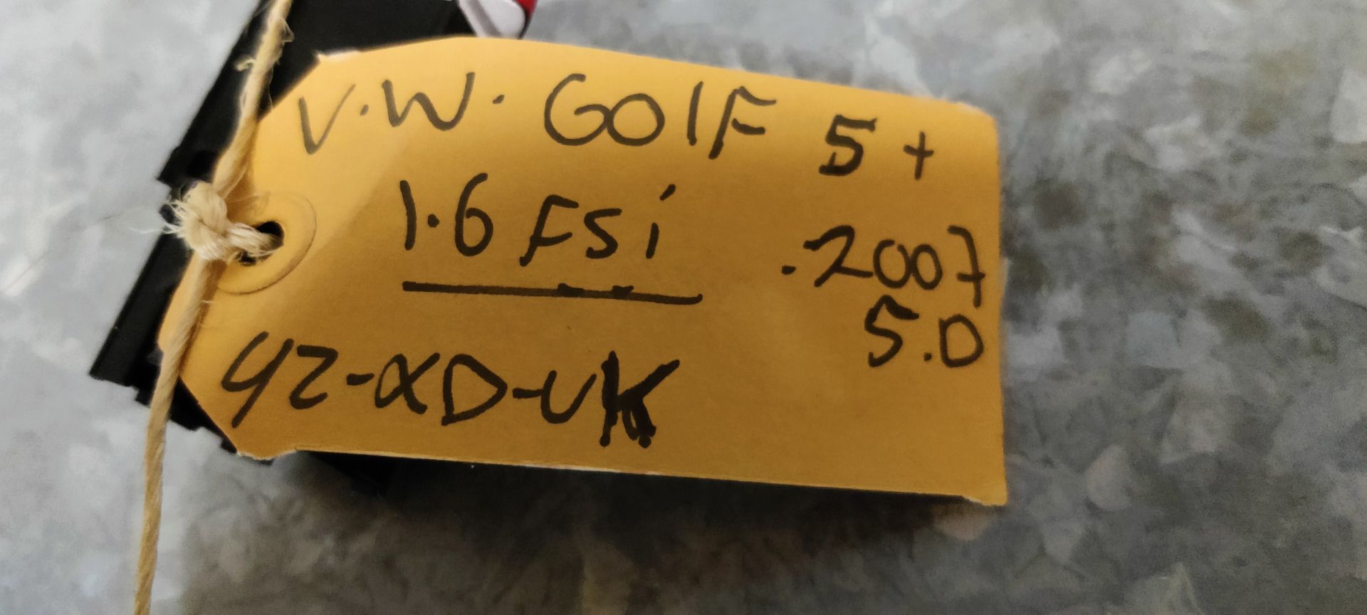 Een rode driehoekige waarschuwingslichtschakelaar met een wit pictogram en een geel label, geplaatst op een metalen oppervlak.