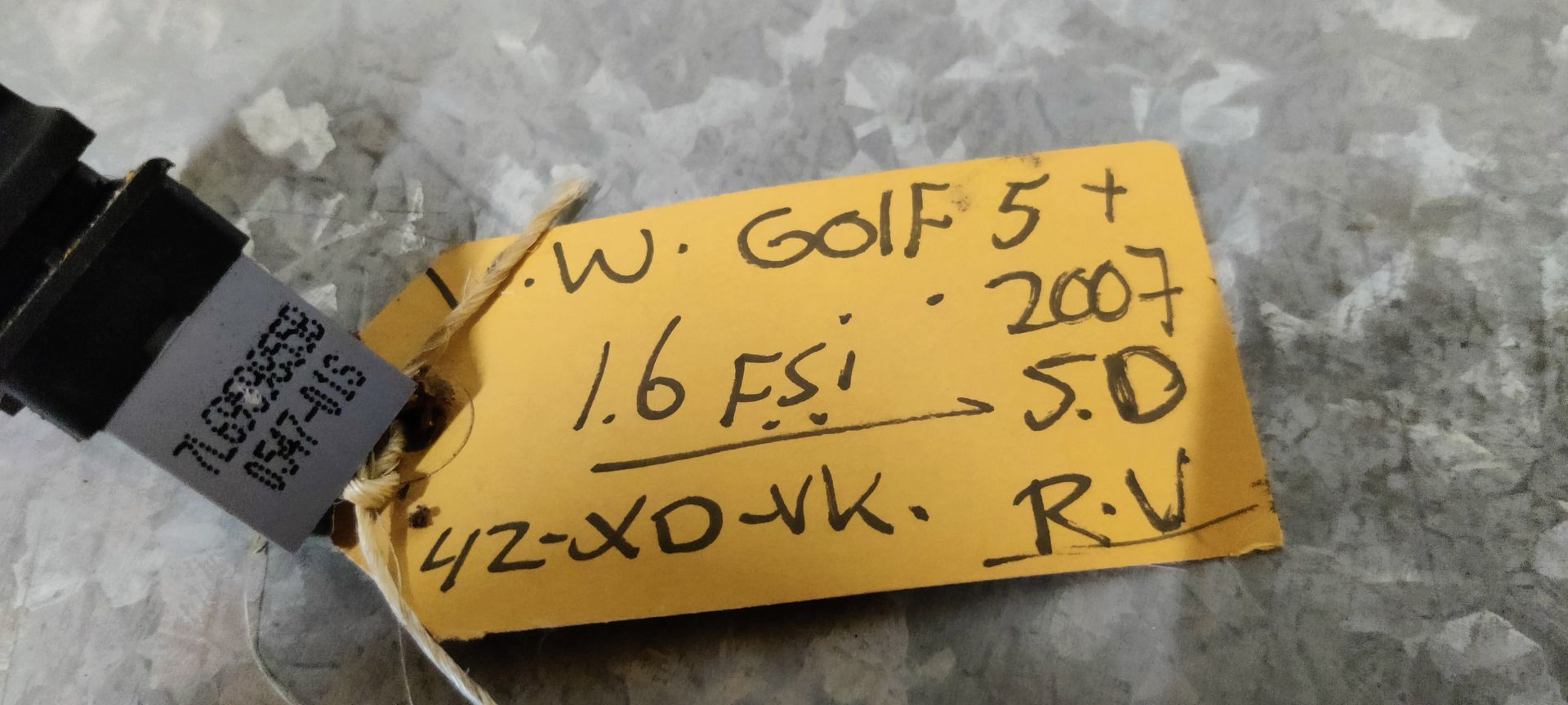 Een enkele zwarte Volkswagen-schakelaar voor de elektrische ramen, voorzien van een wit raamicoon, rustend op een grijs, gestructureerd oppervlak.