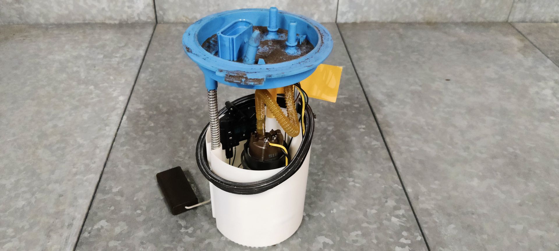 Een brandstofpompunit voor auto's met een blauwe ronde dop, een wit plastic reservoir en een zwarte vlottersensor.