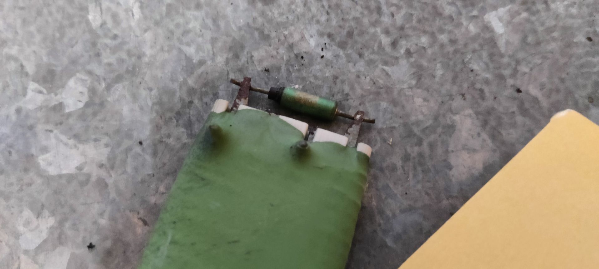 Een groene weerstand voor de ventilator van de airconditioning van een Volkswagen Golf 5 uit 2007, met een witte plastic connector op een metalen oppervlak.