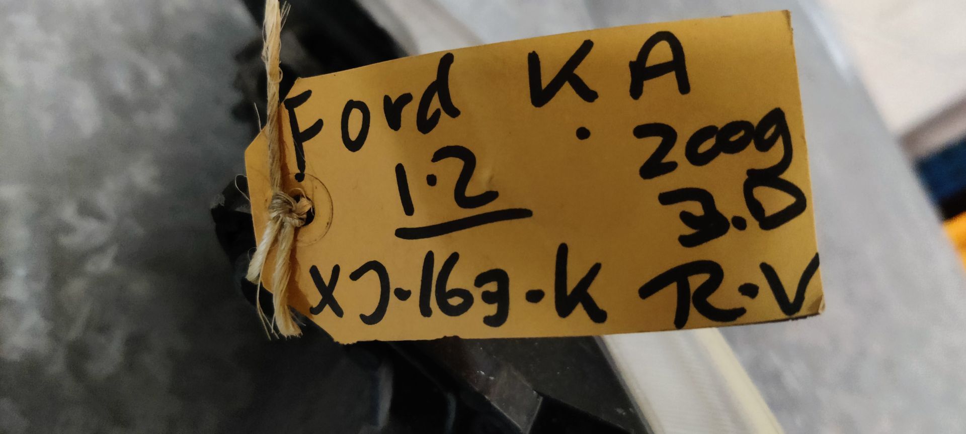 Een gebogen autokoplampunit met een heldere lens en interne reflector, geplaatst op een grijze tegelondergrond.