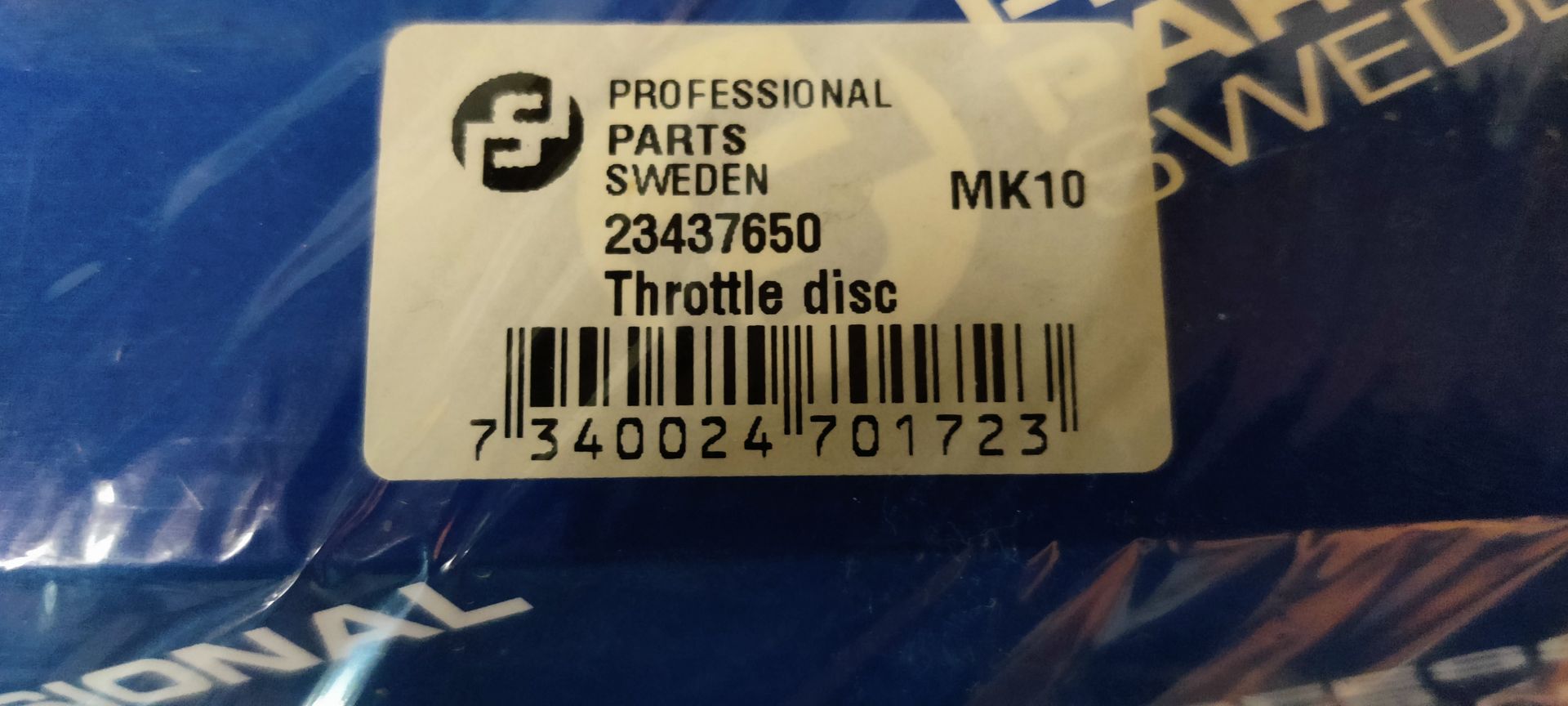 Een verzegelde blauw-witte verpakking met een distributiekettingrevisieset voor auto's, op een grijze betonnen ondergrond.