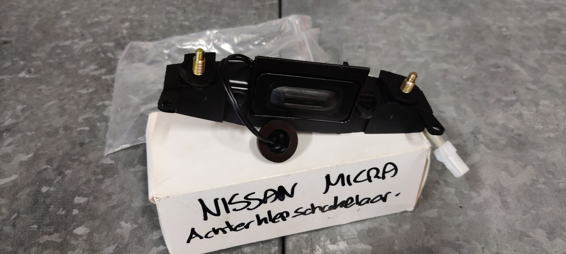 Een zwarte Nissan Micra achterklephendel met schakelaar, liggend op de witte kartonnen doos.