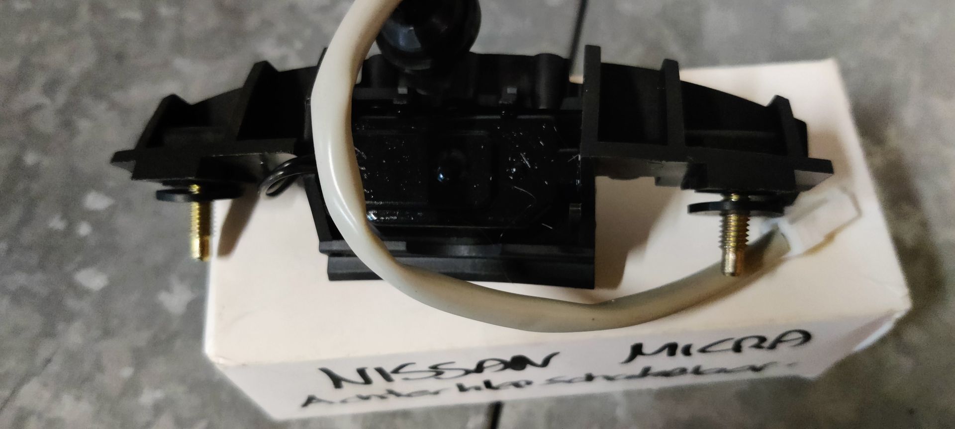 Een zwarte Nissan Micra achterklephendel met schakelaar, liggend op de witte kartonnen doos.