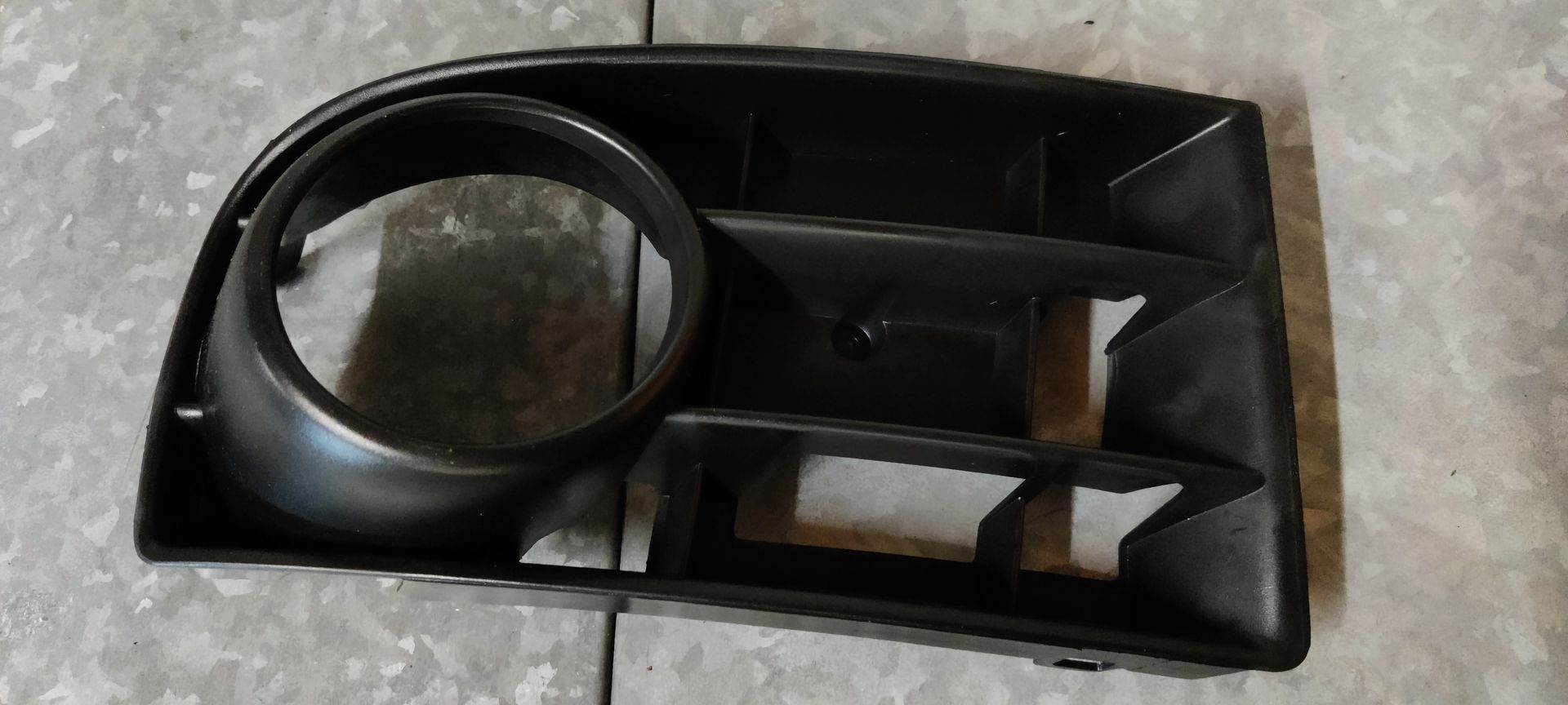 Een zwarte plastic afdekking voor de mistlampgrille van de voorbumper van een auto.