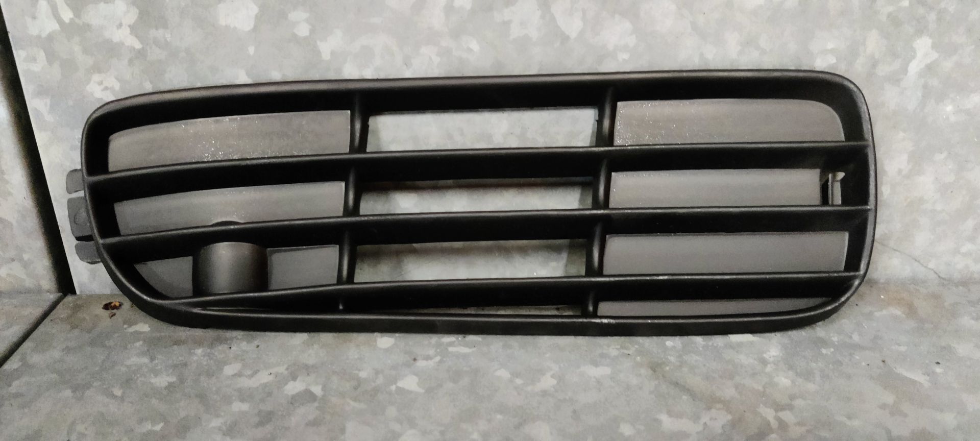 Een zwart, rechthoekig grille van kunststof voor autobumpers, met drie horizontale lamellen en een ronde uitsparing voor een sensor aan één kant.