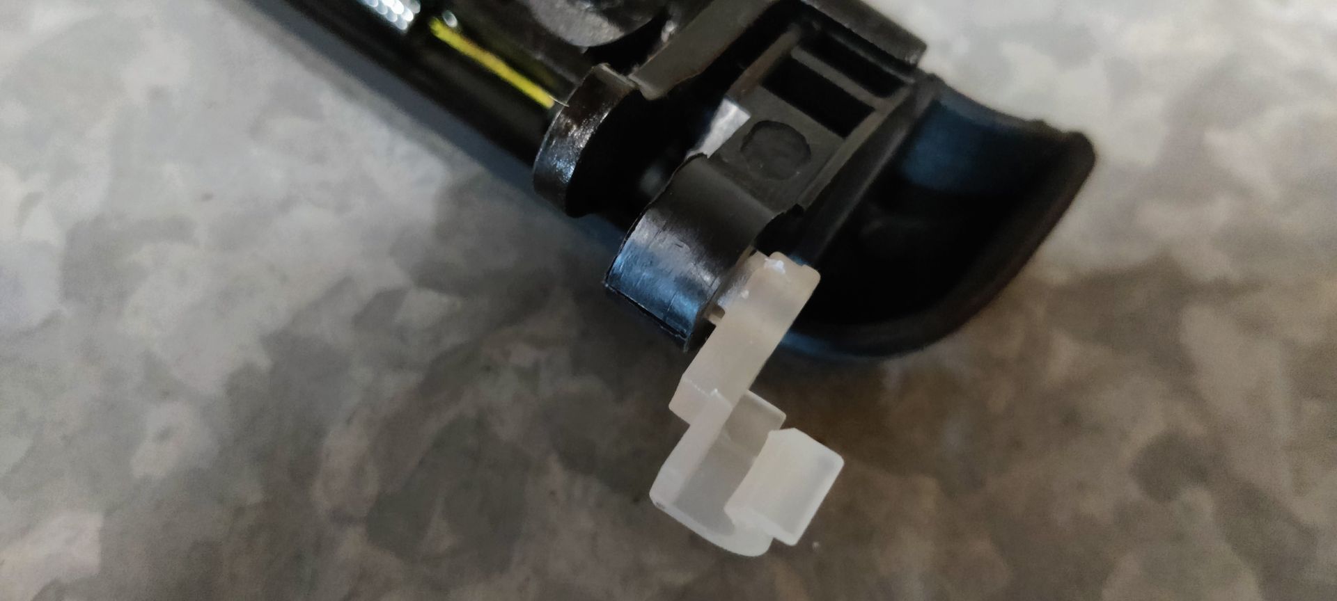 Een matzwarte buitendeurhendel van een auto, rustend op de plastic verpakking tegen een grijze, gestructureerde ondergrond.